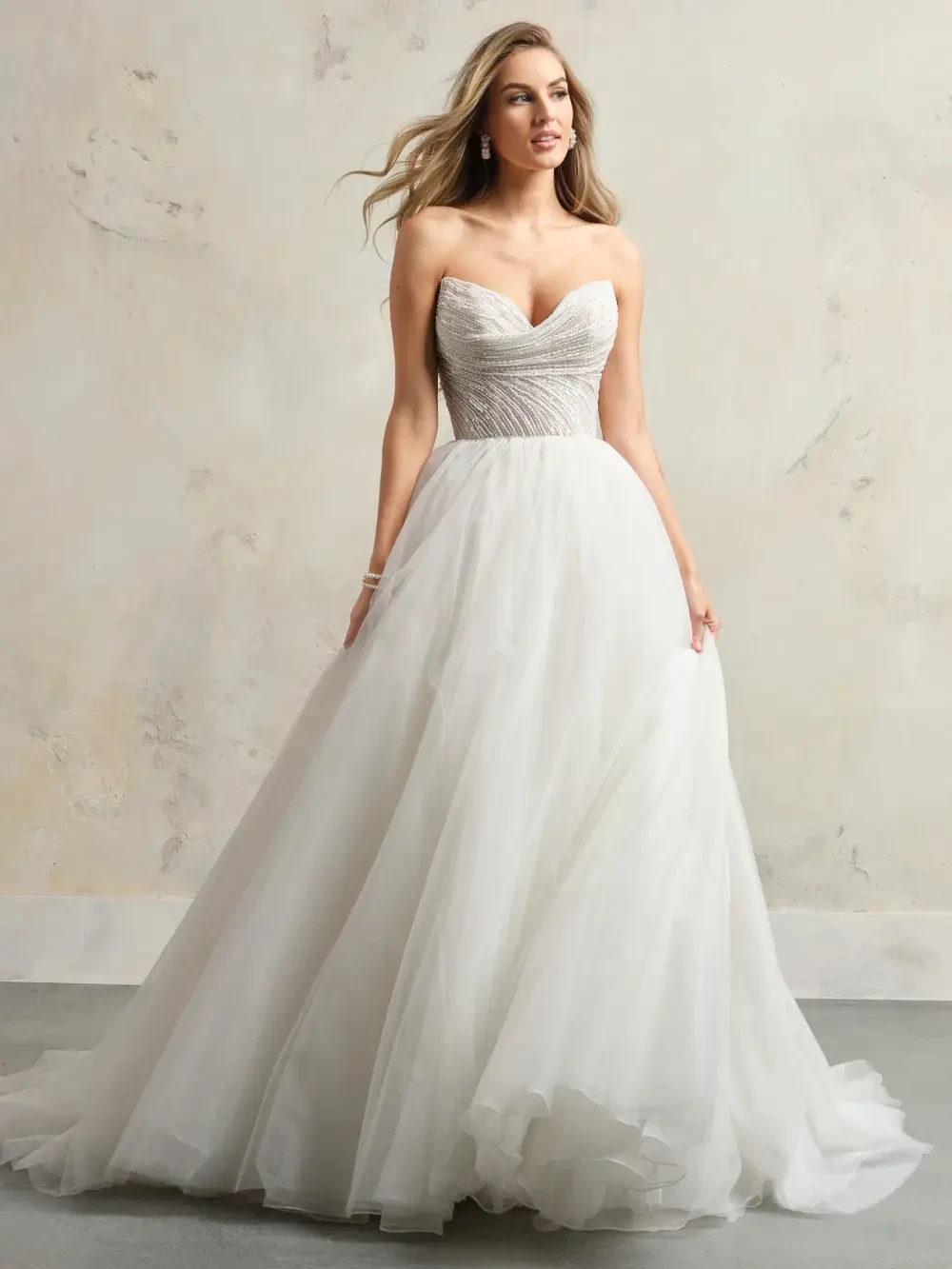 A woman wearing a strapless, embellished white ball gown stands gracefully against a neutral background.