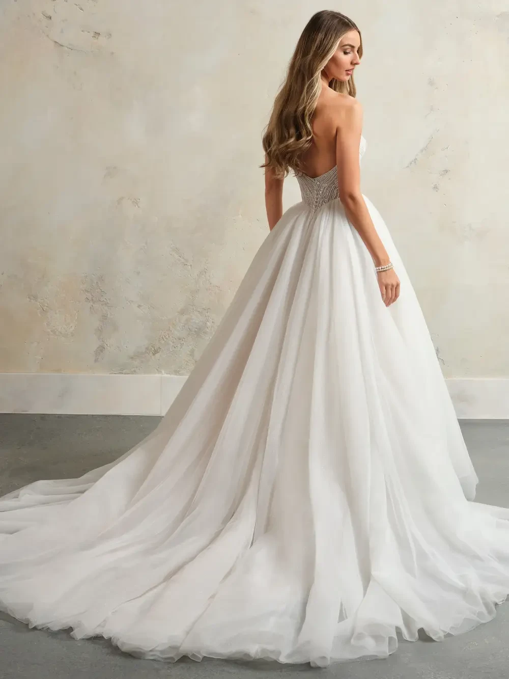 A woman wearing a strapless, embellished white ball gown stands gracefully against a neutral background.