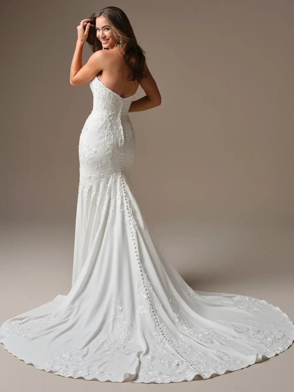 A model wearing a elegant white wedding gown with intricate embroidery, posing against a neutral background.